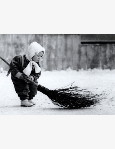 Pieni lapsi lakaisee lumista pihaa luudalla